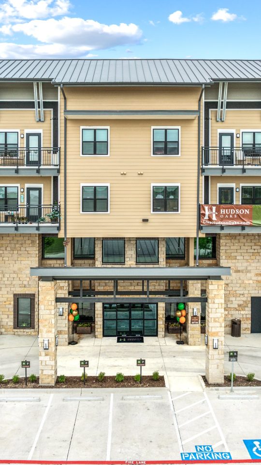 the front of an apartment building with parking lot at The Hudson Oaks